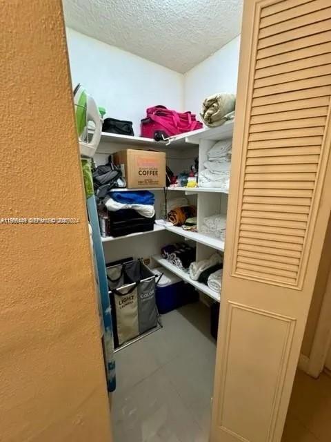 A walk-in closet features white shelving units filled with various household items and storage bins — 1840 Dewey St # 103, Hollywood FL 33020, HOLLYWOOD, FL