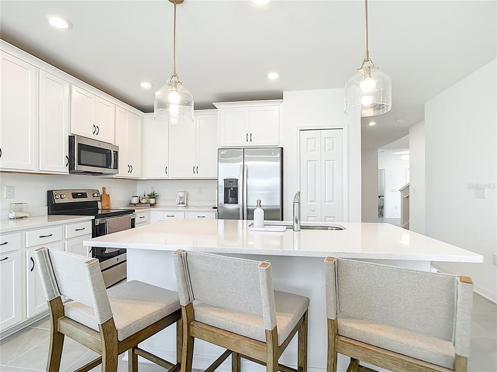 A bright kitchen features white cabinetry, stainless steel appliances, a quartz island, and three chairs — 16863 FIESTA DRIVE, PORT CHARLOTTE, FL