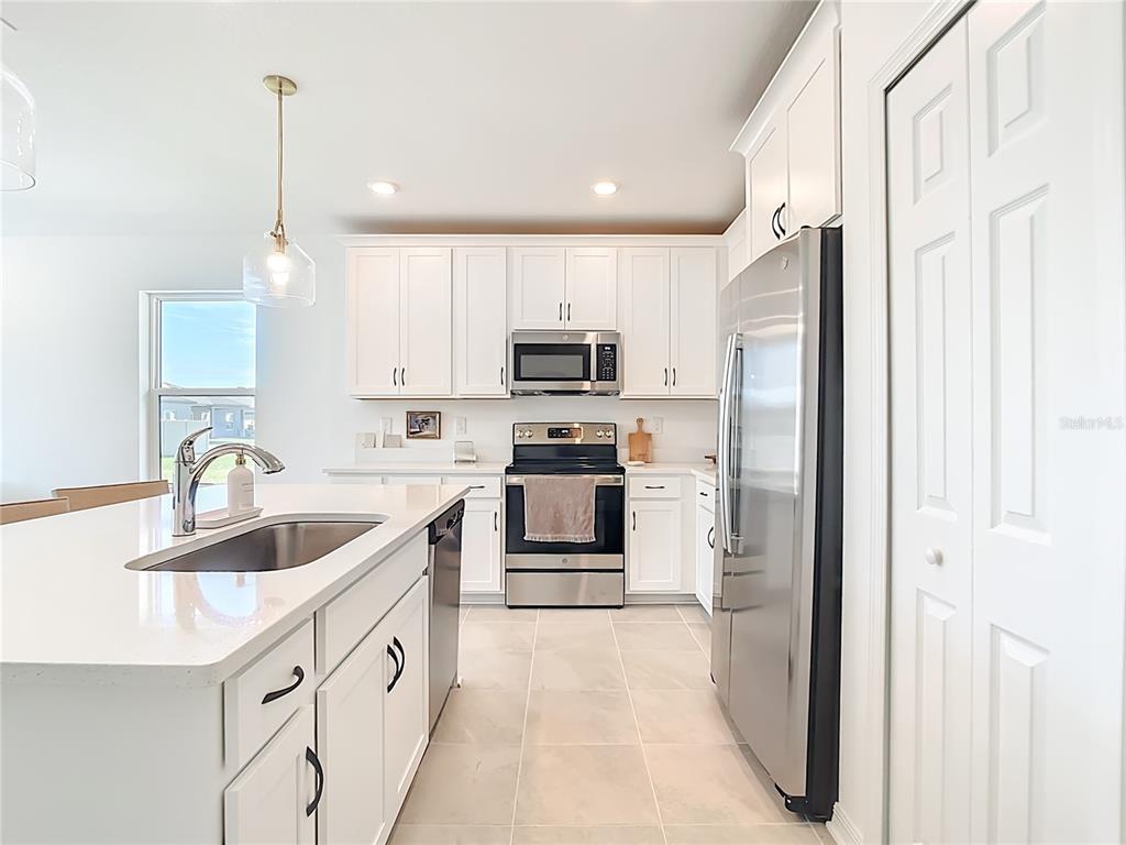 A modern kitchen features white cabinetry, stainless steel appliances, a center island, and tile flooring — 16863 FIESTA DRIVE, PORT CHARLOTTE, FL
