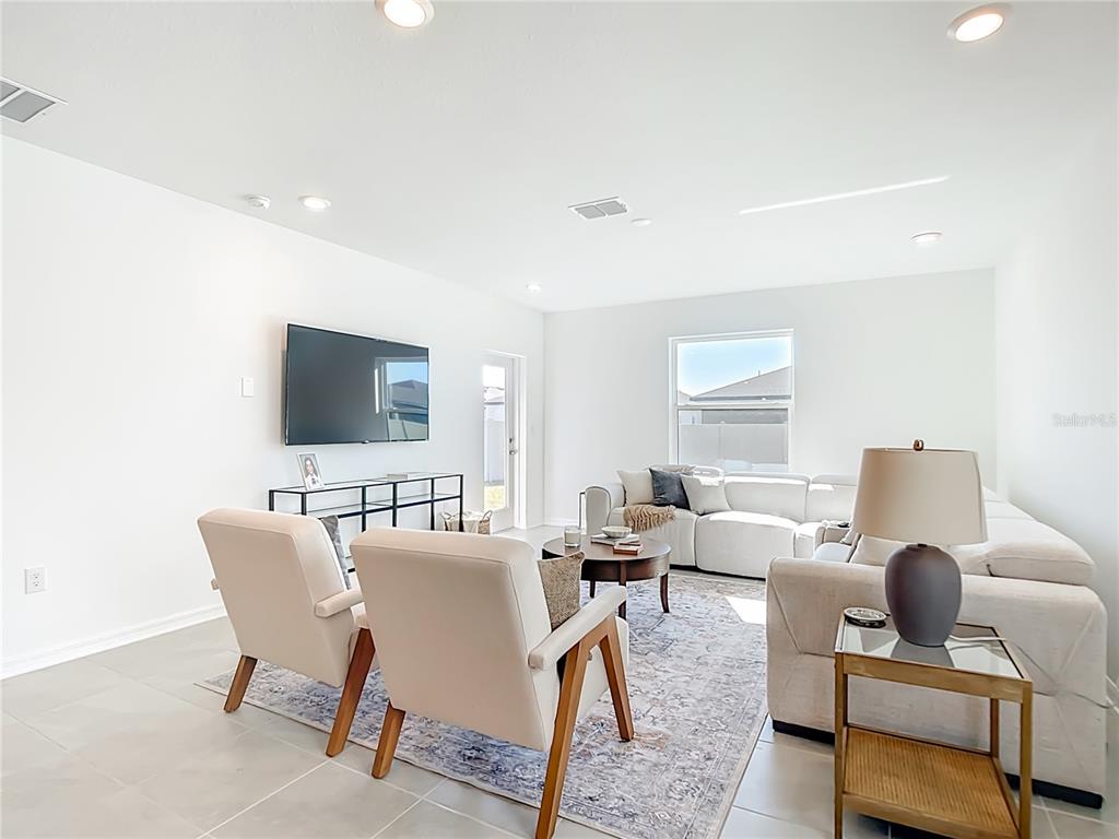 A bright living room features a large sectional sofa, two armchairs, and a wall-mounted television — 16863 FIESTA DRIVE, PORT CHARLOTTE, FL