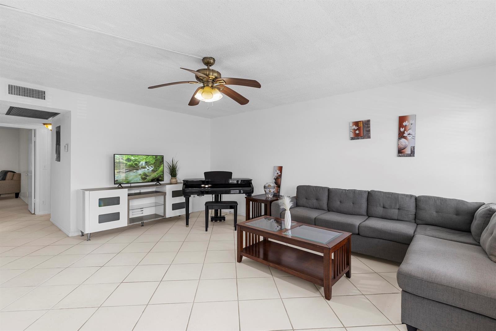 A living room features a gray sectional sofa, a piano, a television console, and tile flooring — 3028 Harwood D, Deerfield Beach FL 33442, DEERFIELD BEACH, FL