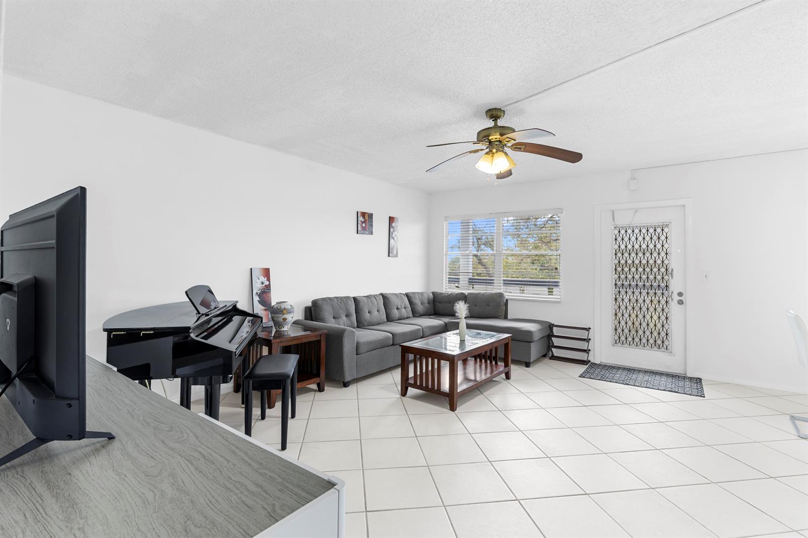 A living room features a grey sectional sofa, a black piano, and white tile flooring — 3028 Harwood D, Deerfield Beach FL 33442, DEERFIELD BEACH, FL
