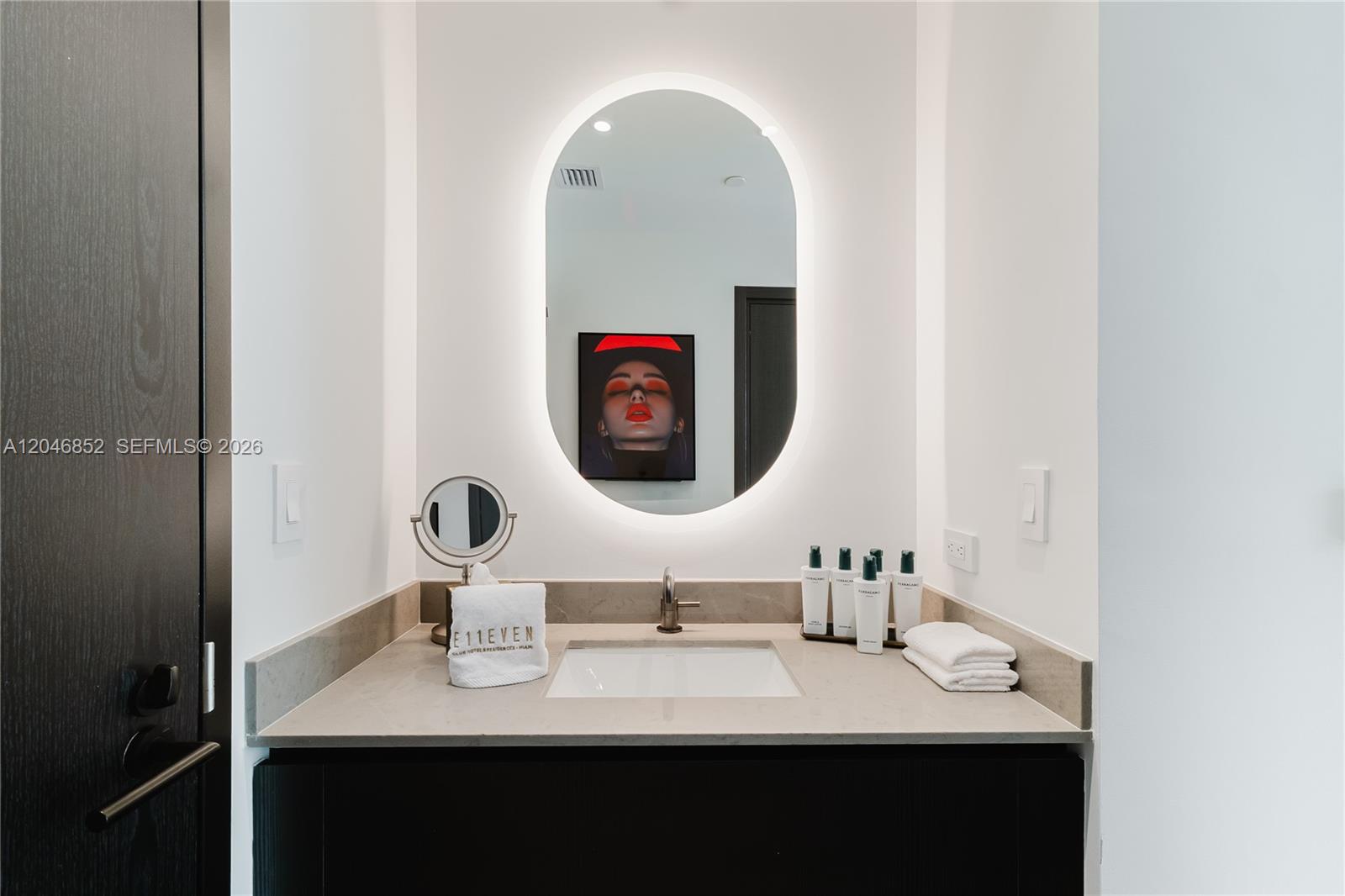 A modern bathroom features a vanity with a stone countertop, oval mirror, and dark cabinetry — 20 NE 11th st # 4907A, Miami FL 33132, MIAMI, FL