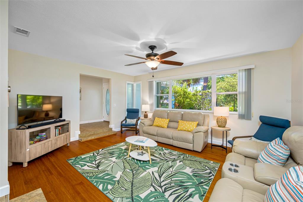 A living room features hardwood floors, a tropical area rug, leather furniture, and large windows — 3749 MCKAY CREEK DRIVE, LARGO, FL