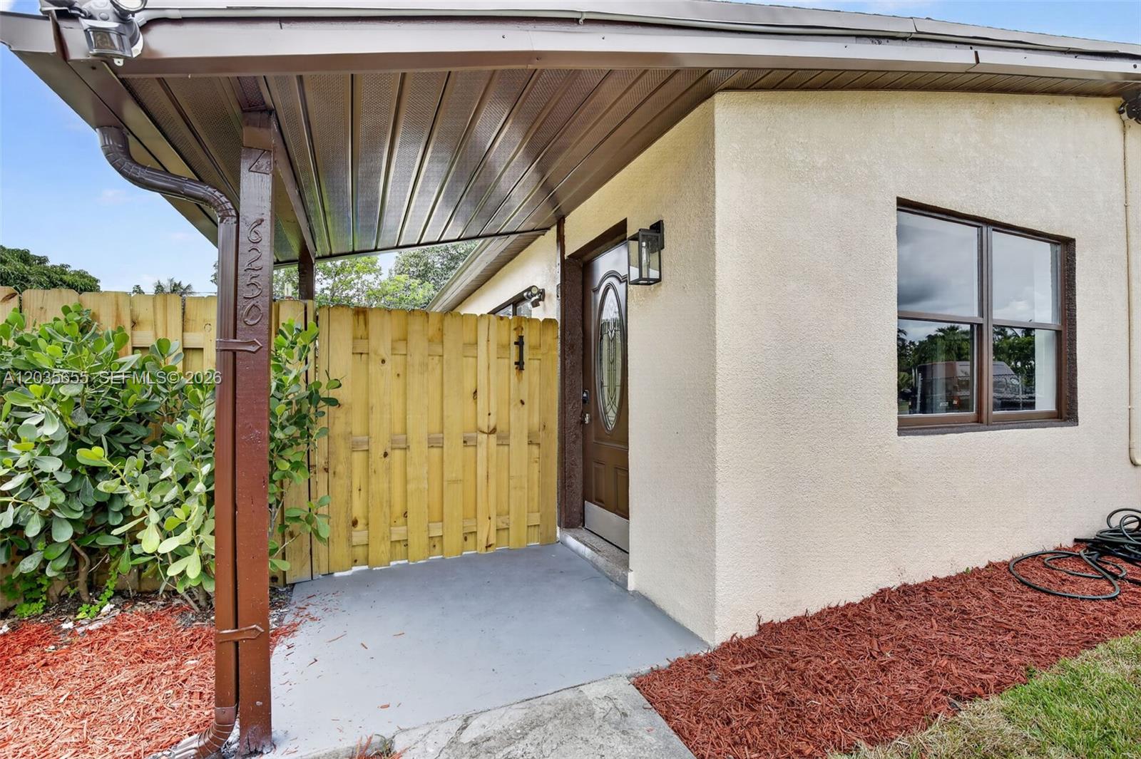 A house exterior features a covered entryway, a wooden fence, and a brown front door — 6250 NW 14th St, Sunrise FL 33313, SUNRISE, FL