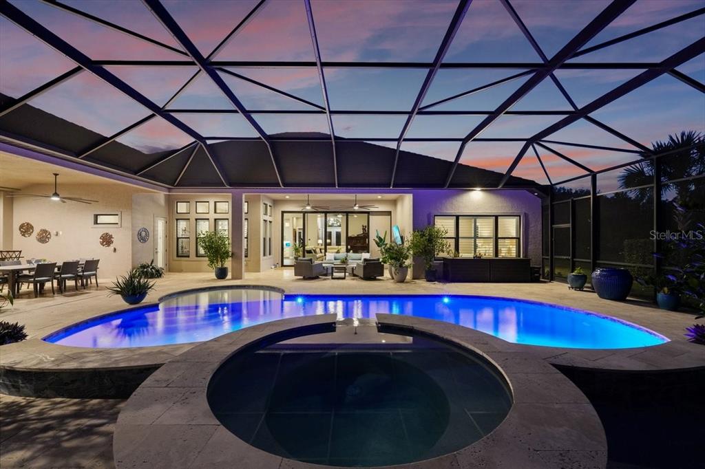A screened-in patio features a swimming pool, a circular spa, and outdoor seating at dusk — 229 CONSERVATORY DRIVE, PALM COAST, FL