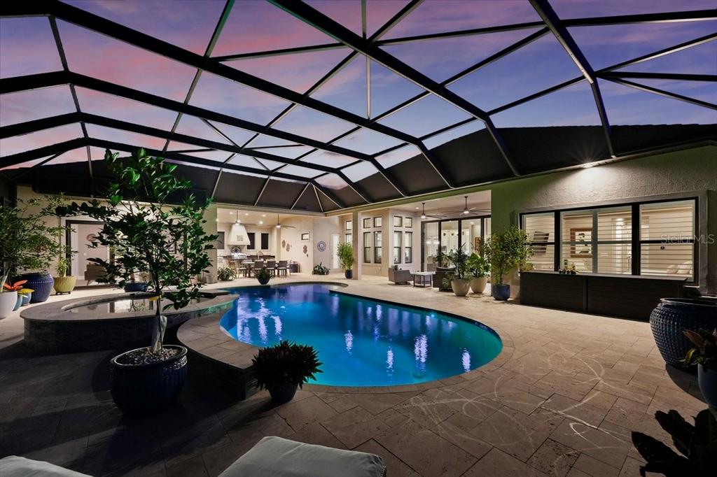 A screened-in patio features a swimming pool, a hot tub, and outdoor seating at dusk — 229 CONSERVATORY DRIVE, PALM COAST, FL
