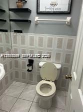 A bathroom features a toilet, tiled walls, black floating shelves, and a white towel bar — 3760 Inverrary Dr # 2R, Lauderhill FL 33319, LAUDERHILL, FL