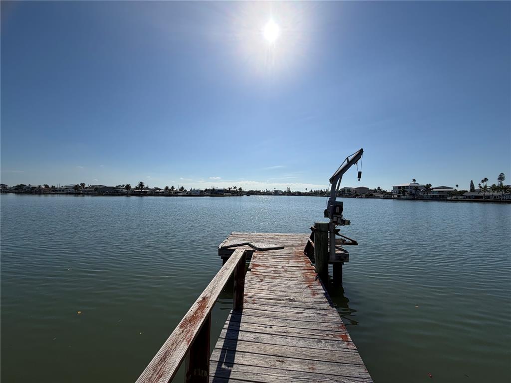 A wooden dock extends into a calm bay under a bright sun with a boat lift — 16325 REDINGTON DRIVE, REDINGTON BEACH, FL