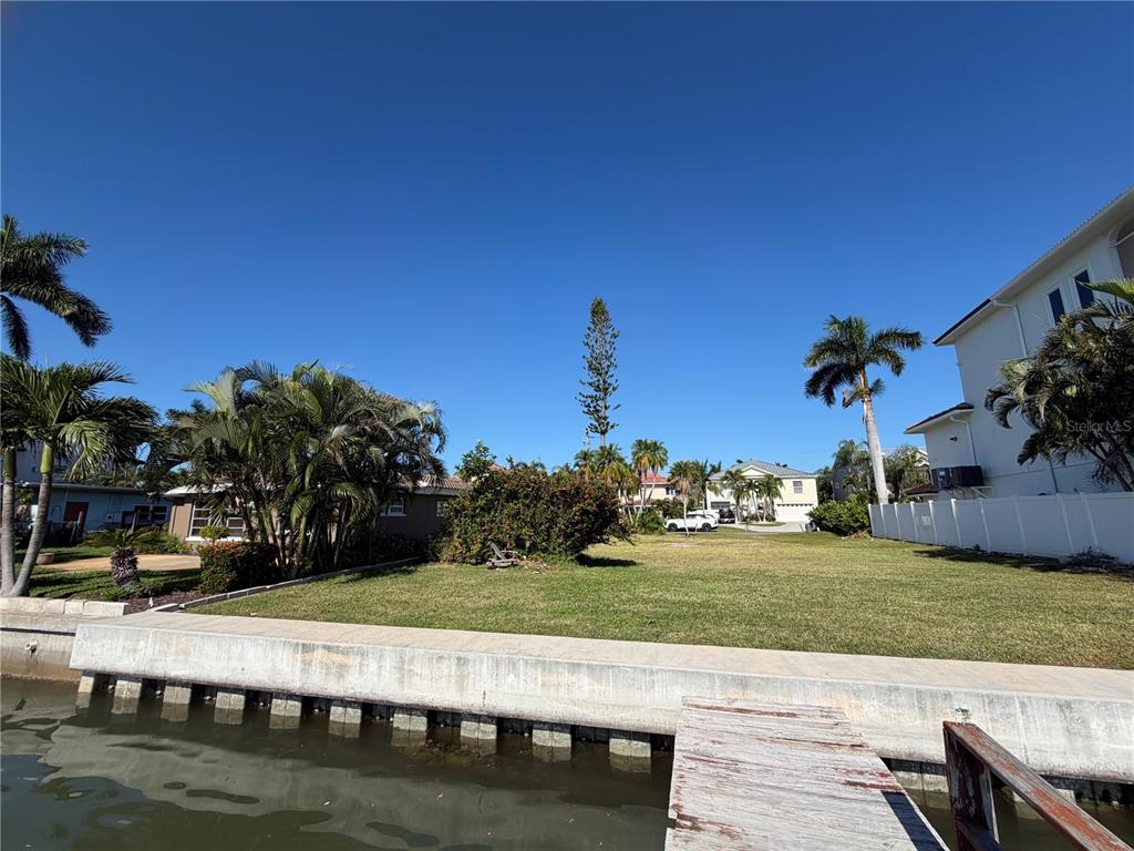 A vacant waterfront lot features a concrete seawall and a wooden dock under a clear sky — 16325 REDINGTON DRIVE, REDINGTON BEACH, FL