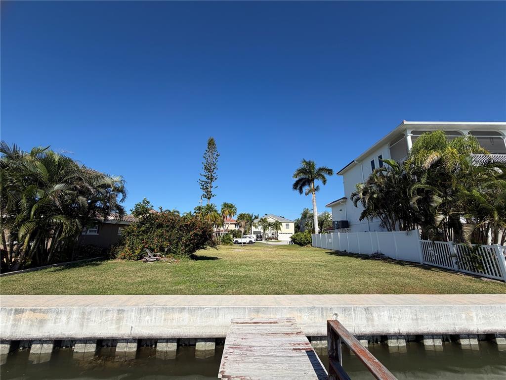 A vacant waterfront lot features a concrete seawall, a wooden dock, and surrounding palm trees — 16325 REDINGTON DRIVE, REDINGTON BEACH, FL