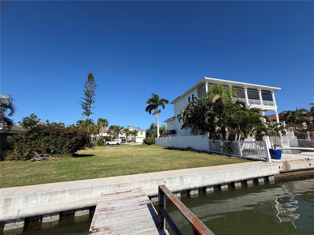 A grassy waterfront lot features a wooden dock, a concrete seawall, and a white house — 16325 REDINGTON DRIVE, REDINGTON BEACH, FL