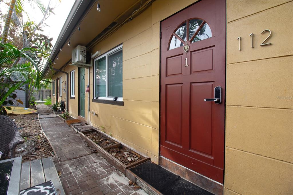 A red front door with a digital lock is on a yellow building exterior — 112 119TH AVENUE, TREASURE ISLAND, FL