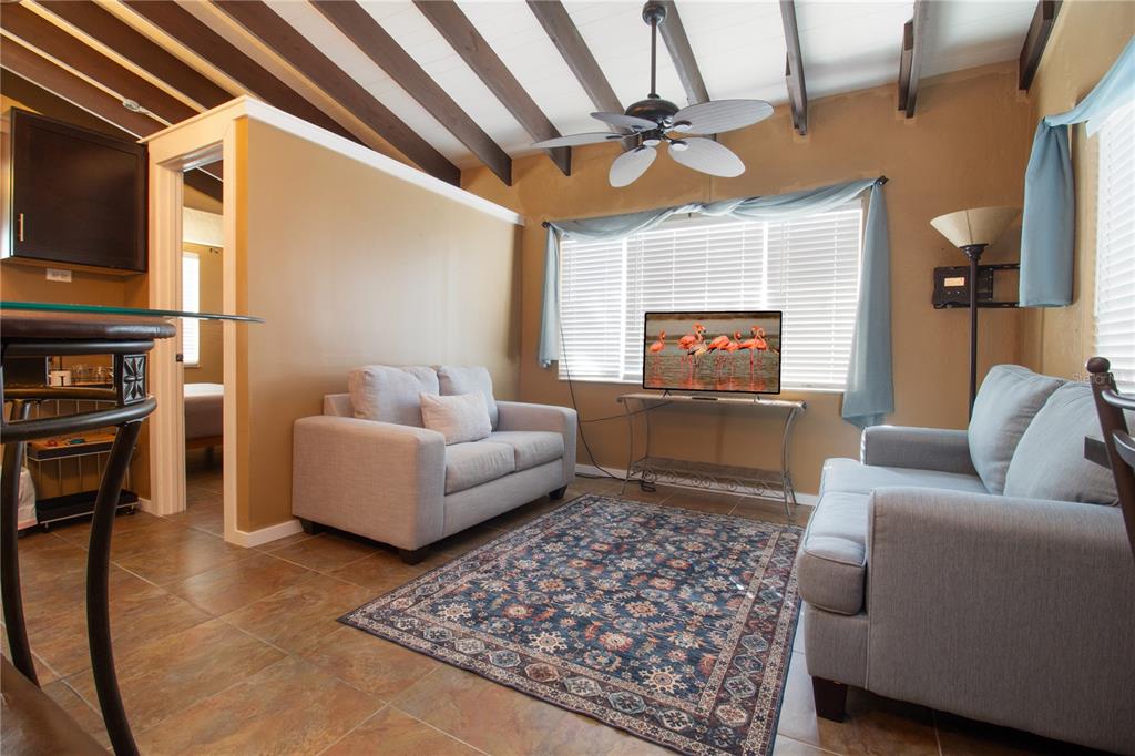 A living room features light gray sofas, a patterned area rug, and exposed ceiling beams — 112 119TH AVENUE, TREASURE ISLAND, FL
