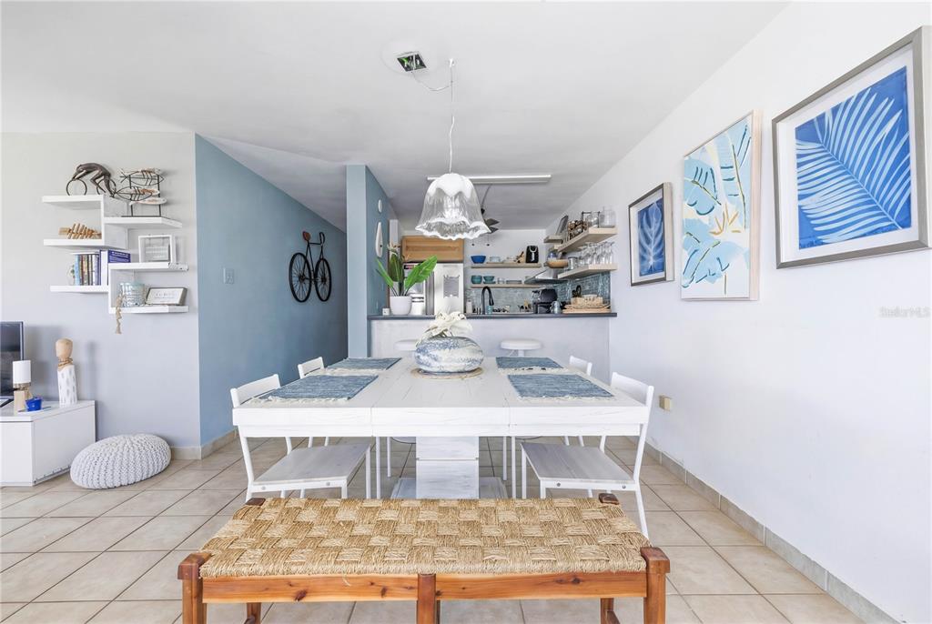 A dining area with a white table and chairs sits in front of an open kitchen — Haudimar Beach Apartments 4466 UNIT F208, ISABELA, PR