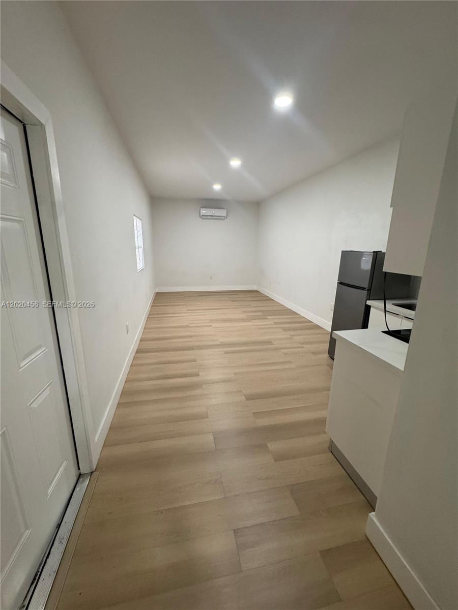 This narrow room features light wood-look flooring, white walls, recessed lighting, and a small kitchenette — MIAMI, FL