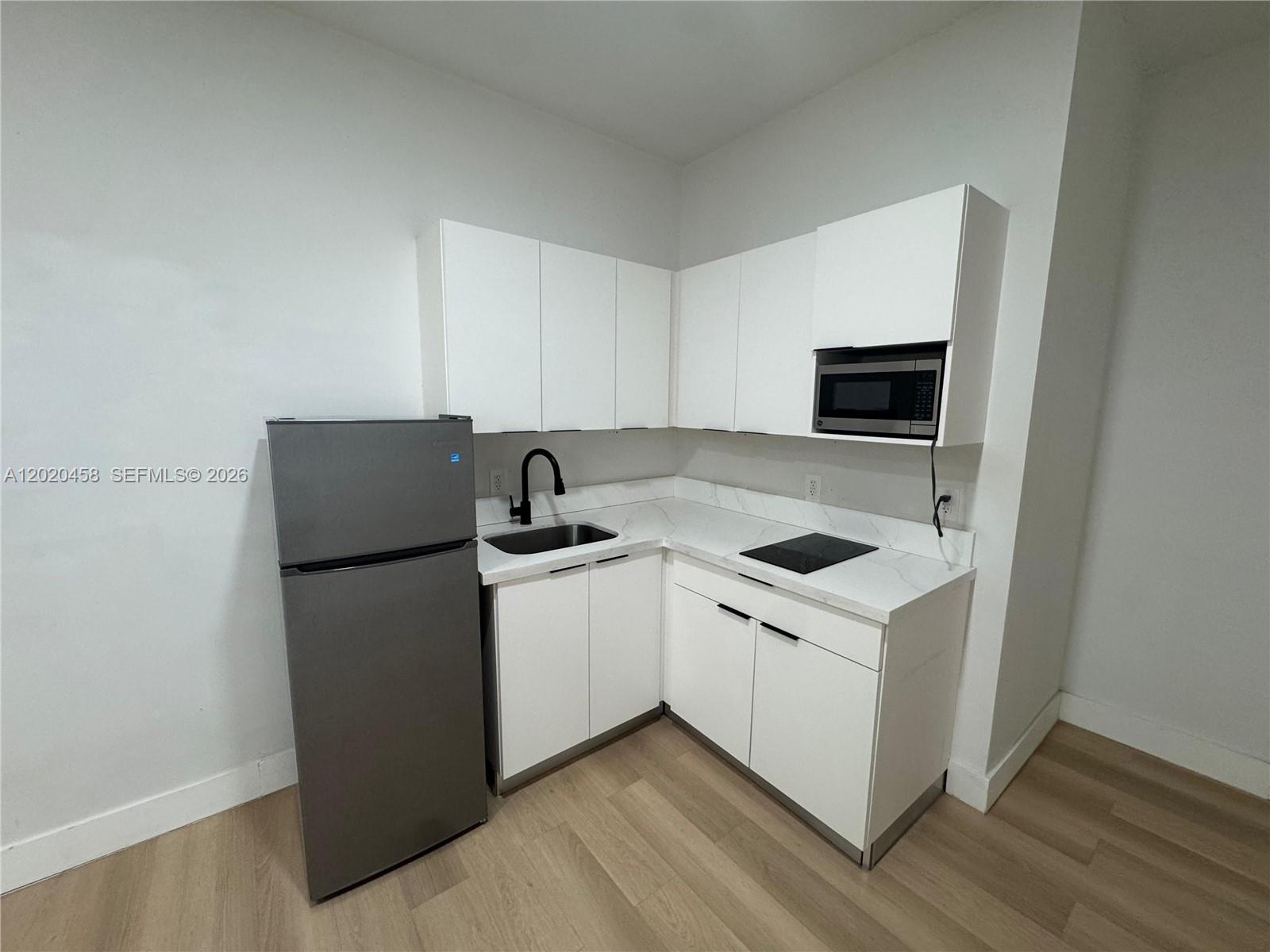 A small kitchen features white cabinets, a grey refrigerator, a black faucet, and white countertops — MIAMI, FL