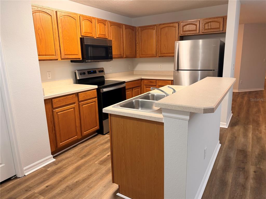 A kitchen features wooden cabinets, stainless steel appliances, a double sink, and light-colored countertops — 3623 CARUSO PLACE, OVIEDO, FL