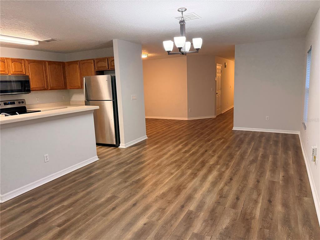 An open-concept kitchen and living area featuring wood-look flooring and a stainless steel refrigerator — 3623 CARUSO PLACE, OVIEDO, FL