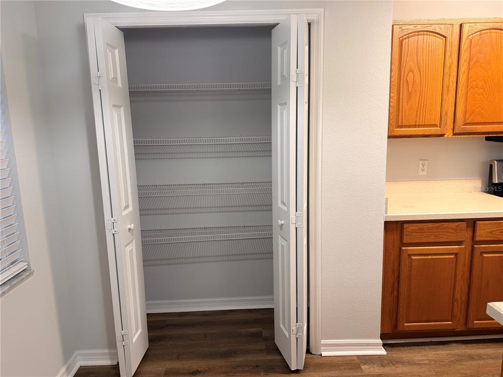 An open pantry with wire shelving sits next to wooden kitchen cabinets and countertops — 3623 CARUSO PLACE, OVIEDO, FL