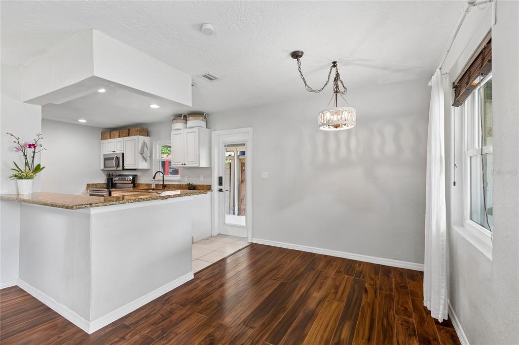 A dining area with wood floors and a chandelier adjacent to an open-concept kitchen — 3912 W LEILA AVENUE, TAMPA, FL