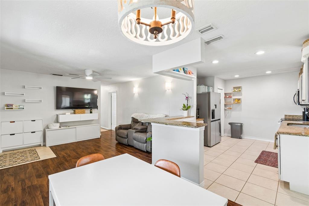 An open-concept living and dining area features wood flooring, a kitchen island, and white cabinetry — 3912 W LEILA AVENUE, TAMPA, FL