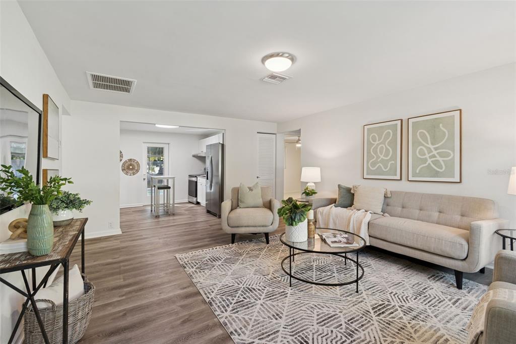 A bright living room features a sofa, armchair, glass coffee table, and a wall-mounted television — 2195 GLEN DRIVE, SAFETY HARBOR, FL