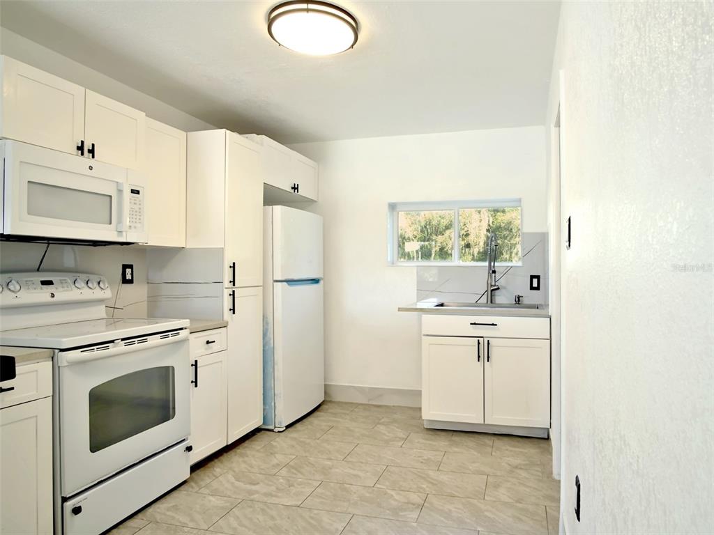 A kitchen features white cabinets, white appliances, a window, and light-colored tile flooring — 15201 BAILEY HILL ROAD, BROOKSVILLE, FL