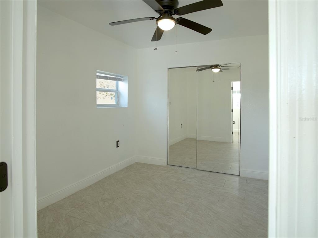 A bedroom with white walls, tile flooring, a ceiling fan, and mirrored closet doors — 15201 BAILEY HILL ROAD, BROOKSVILLE, FL