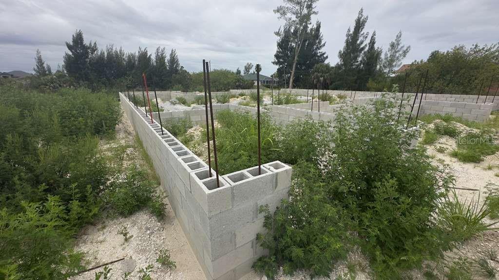 An unfinished concrete block foundation stands on a grassy, overgrown residential lot — 15408 LAKELAND CIRCLE, PORT CHARLOTTE, FL