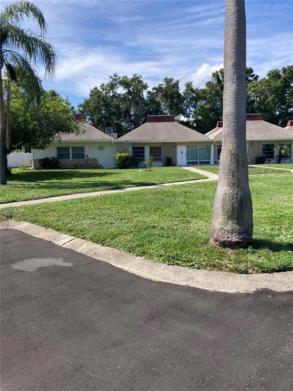 A single-story residential building with a hip roof sits behind a lawn and palm tree — 4313 TAHITIAN GARDENS CIRCLE CIRCLE UNIT B, HOLIDAY, FL
