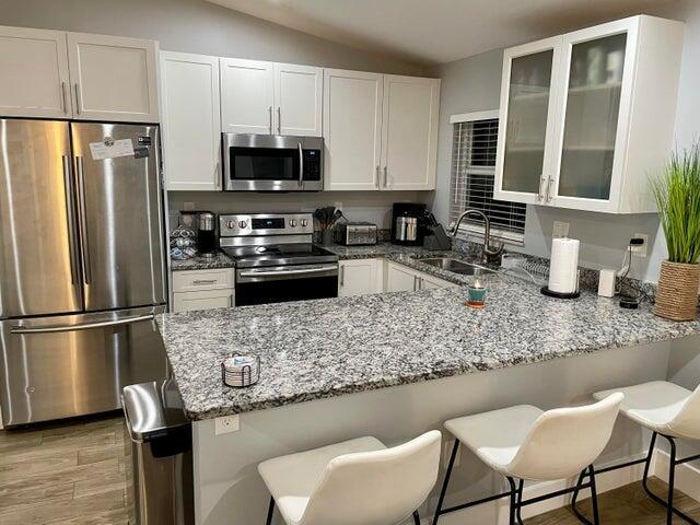 A kitchen features white cabinets, stainless steel appliances, and a granite-topped peninsula with bar stools — 601 N E Street, FL 33460, FL