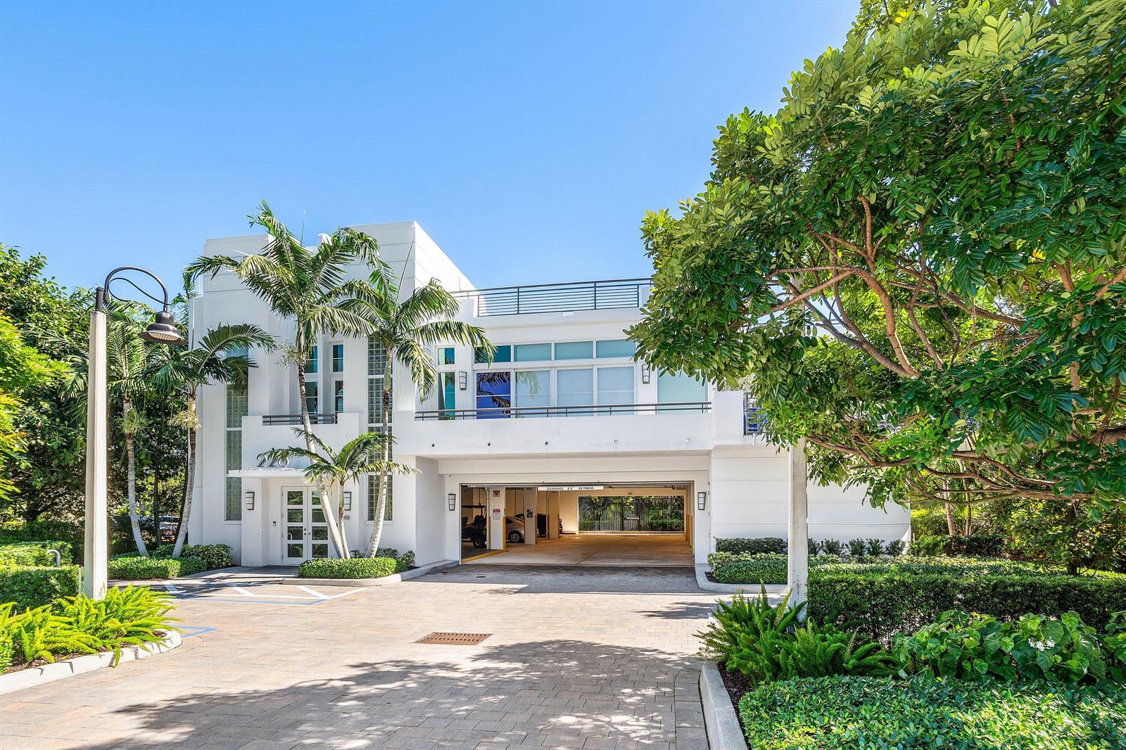 A white two-story building features a ground-level parking garage, palm trees, and a paved driveway — 226 Palm Court, Delray Beach FL 33444, DELRAY BEACH, FL