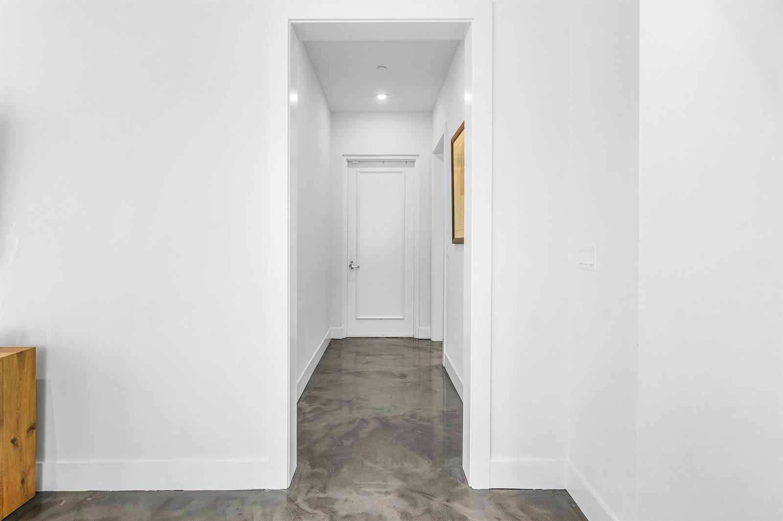 A hallway with white walls and a polished gray concrete floor leads to a door — 226 Palm Court, Delray Beach FL 33444, DELRAY BEACH, FL