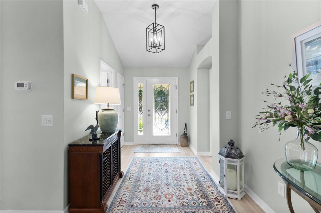 A bright entryway features a patterned rug, a wooden console table, and a glass front door — 2132 SANSORES STREET, THE VILLAGES, FL