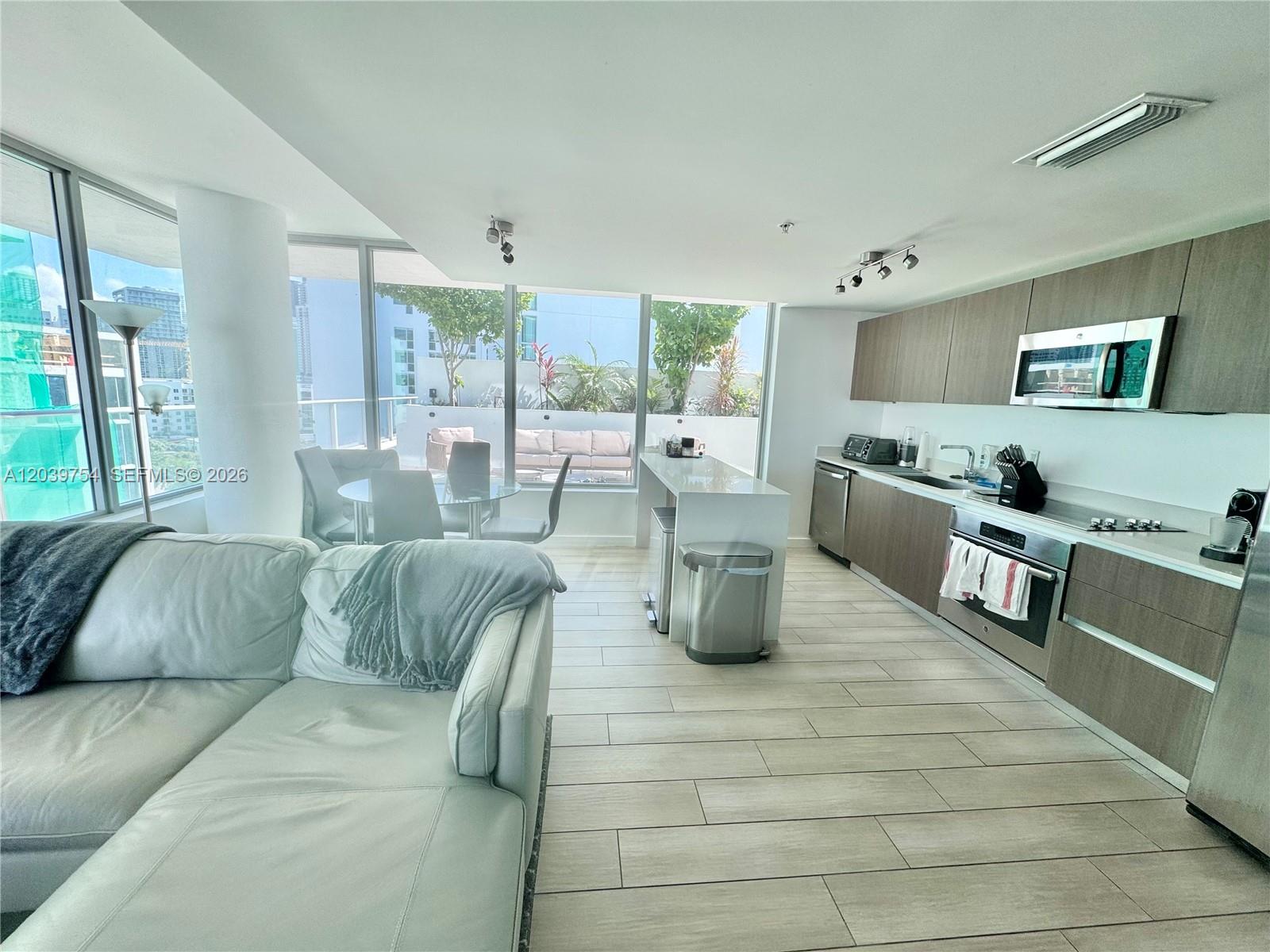 A modern kitchen and living area feature wood cabinetry, stainless appliances, and floor-to-ceiling windows — 1600 SW 1st Ave # 910, Miami FL 33129, MIAMI, FL