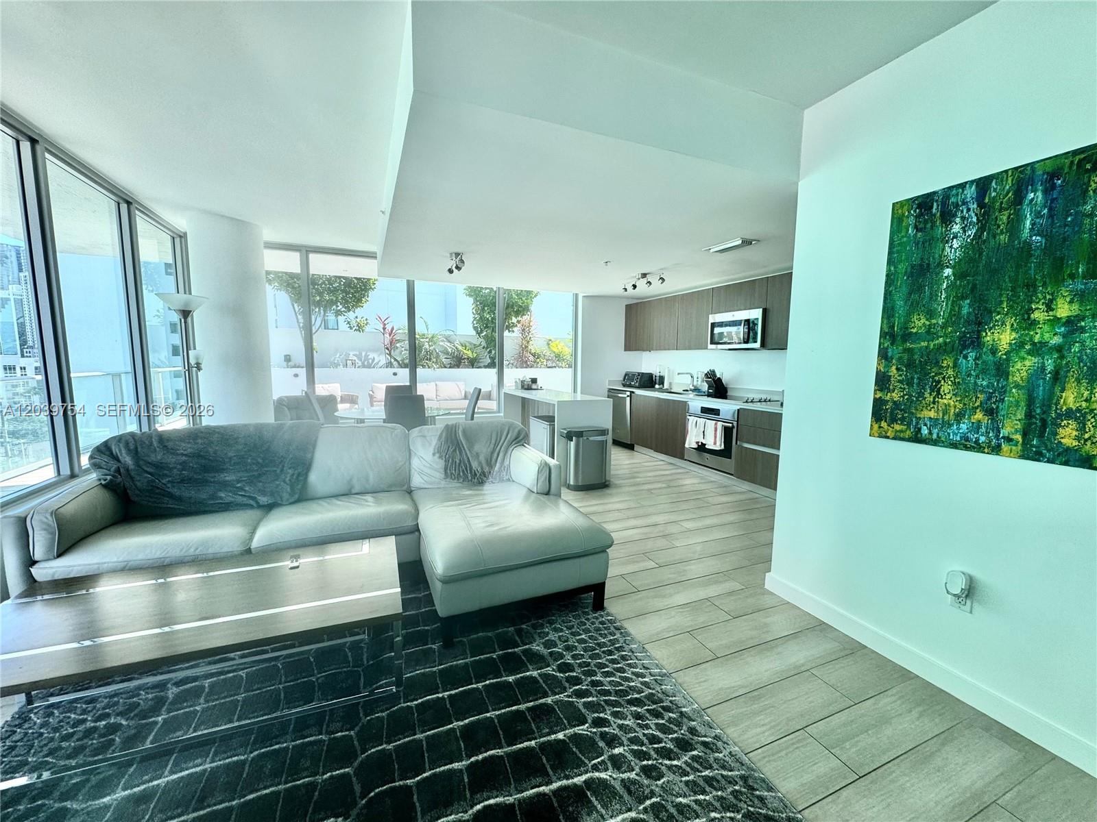 An open-concept living room and kitchen feature light wood-look tile flooring and floor-to-ceiling windows — 1600 SW 1st Ave # 910, Miami FL 33129, MIAMI, FL