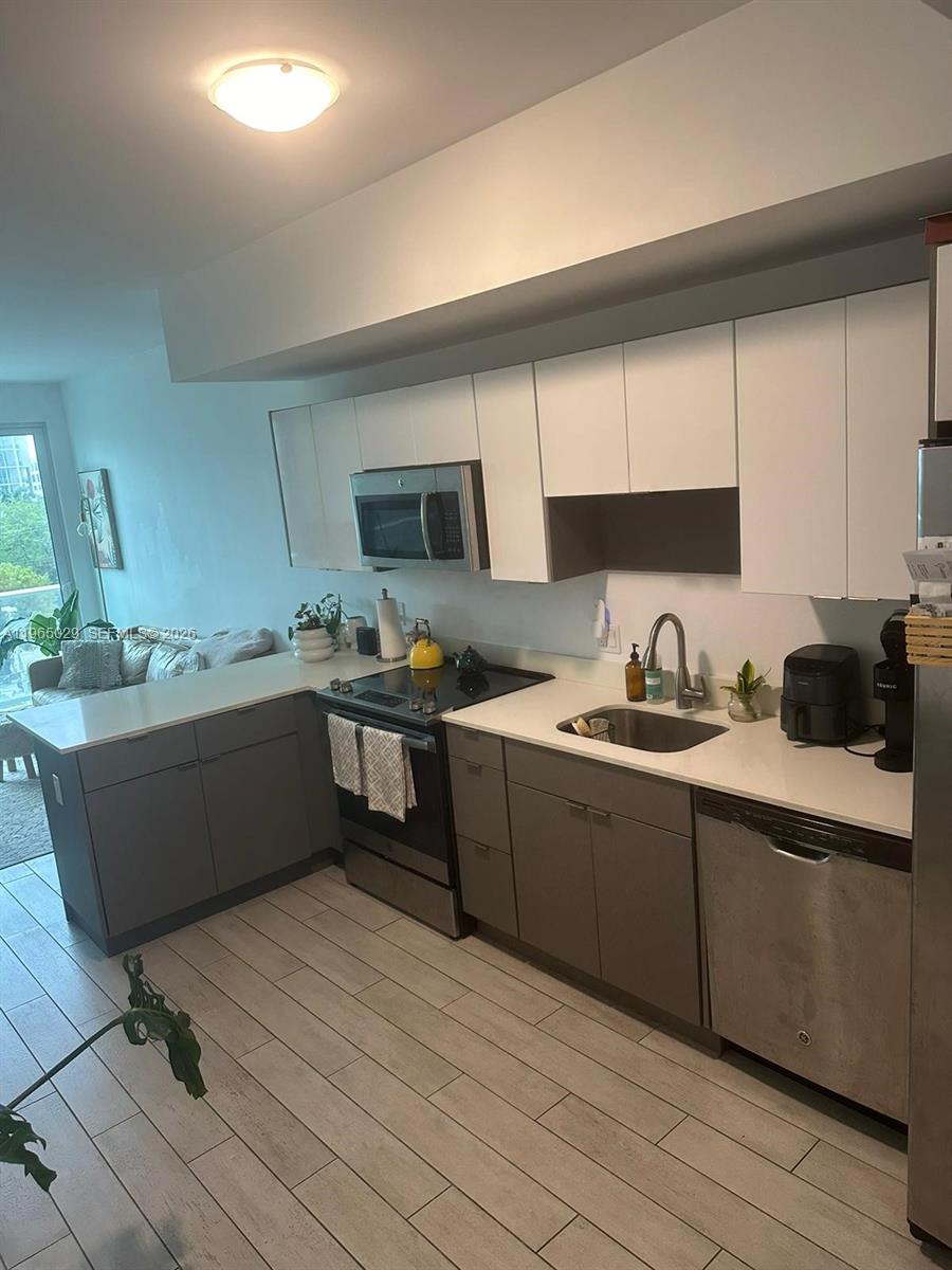 A modern kitchen features white upper cabinets, gray lower cabinets, stainless steel appliances, and tile flooring — 321 NE 26th St # 511, Miami FL 33137, MIAMI, FL