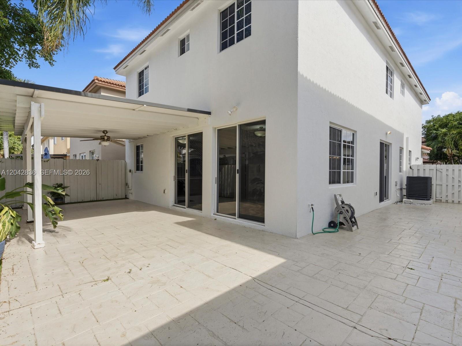 The exterior of a white two-story house features a covered patio and a paved backyard — 11274 NW 43rd Ter, Doral FL 33178, DORAL, FL