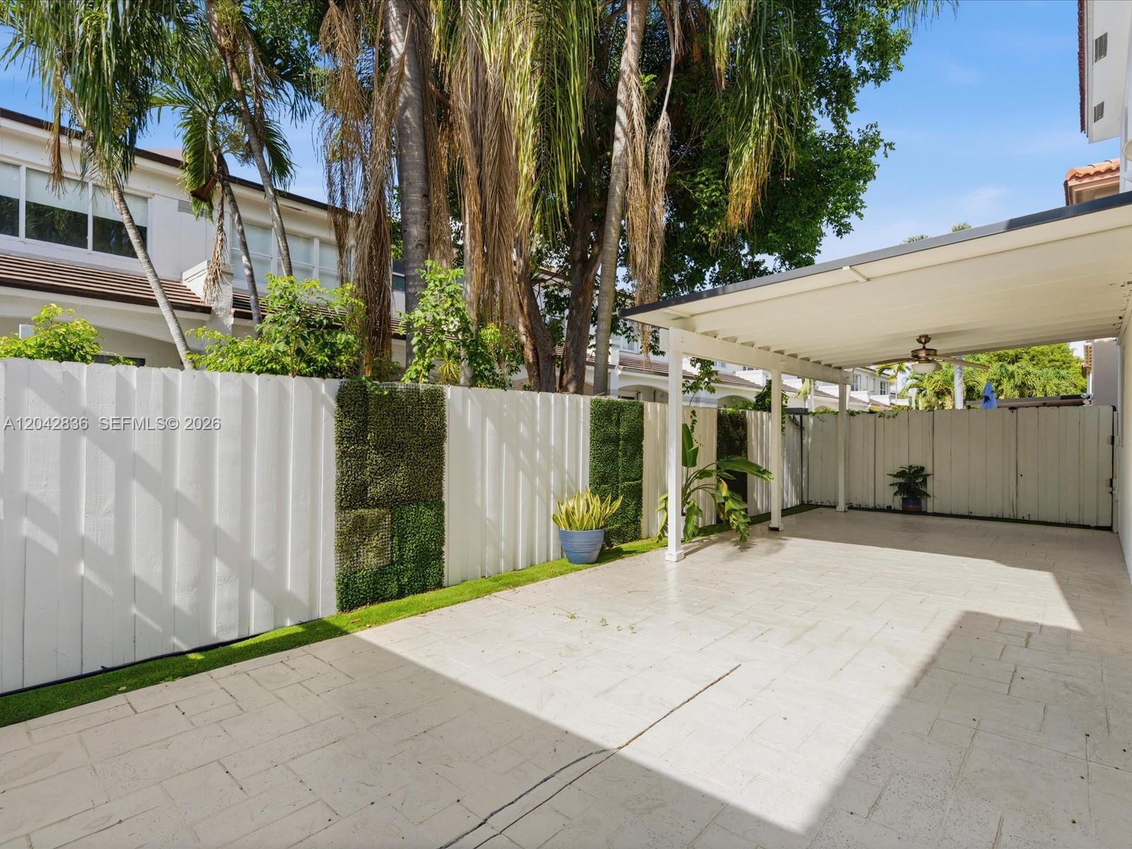 A paved patio area features a white fence with vertical greenery and a covered carport — 11274 NW 43rd Ter, Doral FL 33178, DORAL, FL