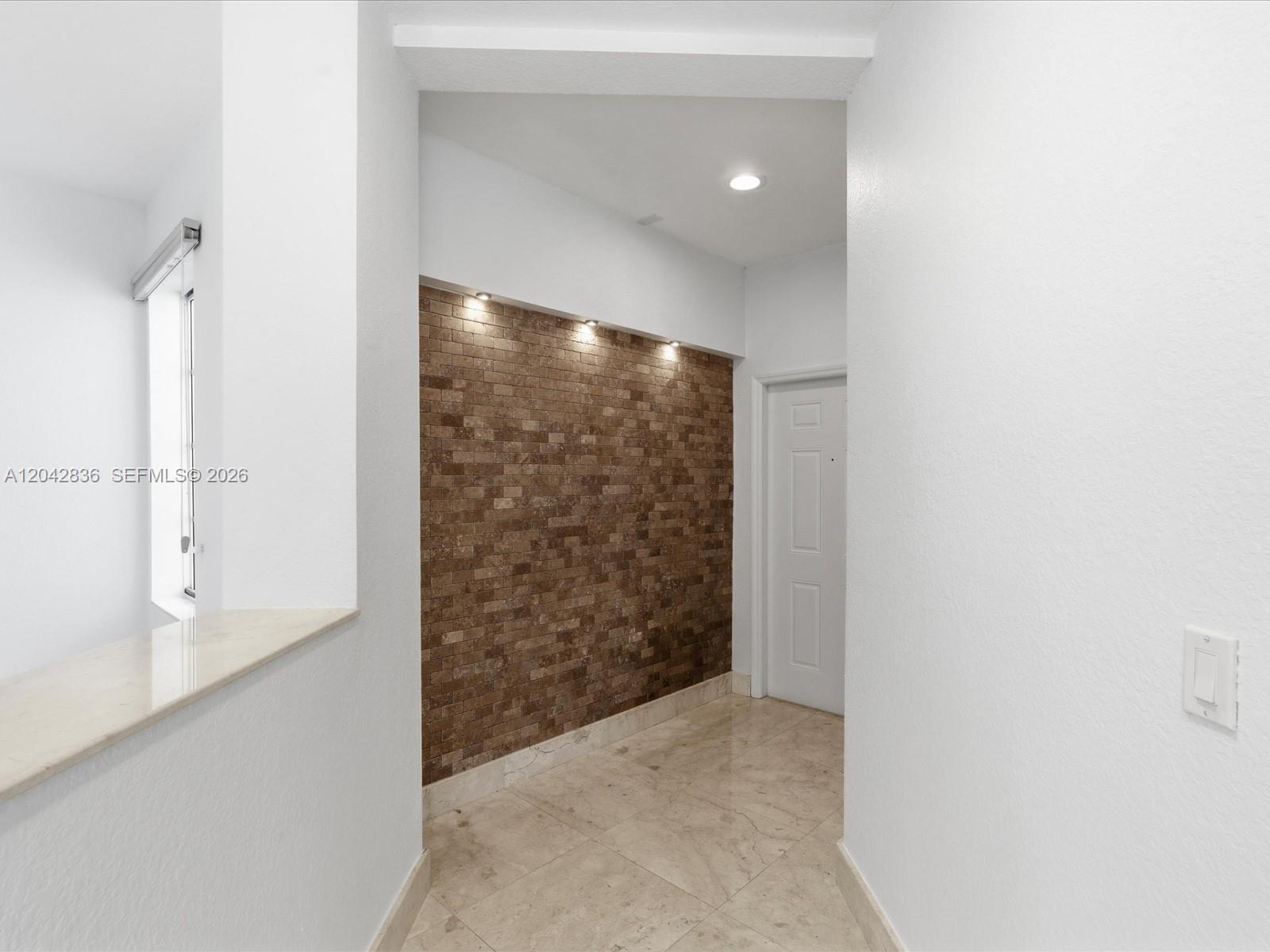 A hallway features a textured brick accent wall with recessed lighting and marble tile flooring — 11274 NW 43rd Ter, Doral FL 33178, DORAL, FL