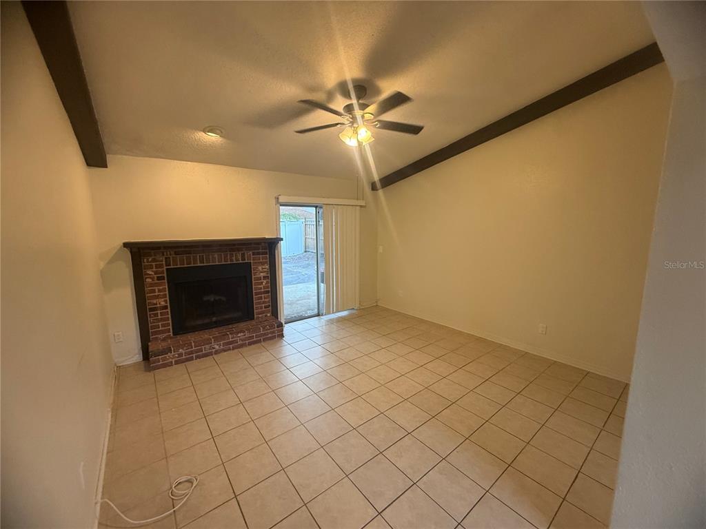 A living room features a brick fireplace, tile flooring, and a vaulted ceiling with beams — 5118 LETITIA COURT, TAMPA, FL