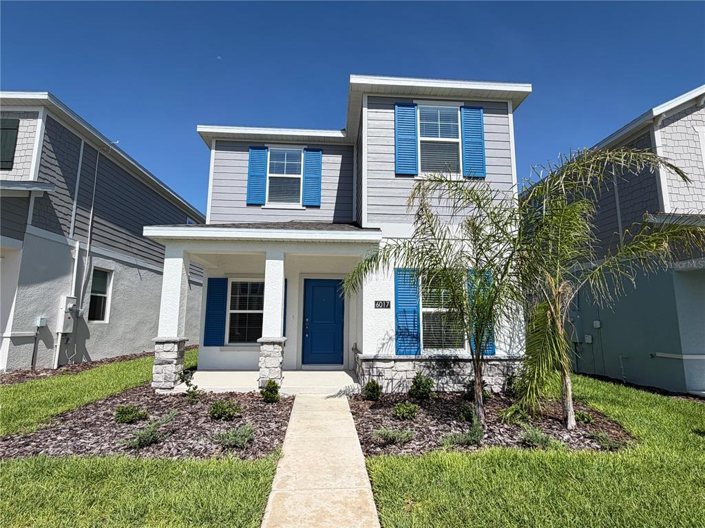 A two-story house with gray siding, blue shutters, and a front porch with stone pillars — 6017 WELLBEING WAY, CLERMONT, FL
