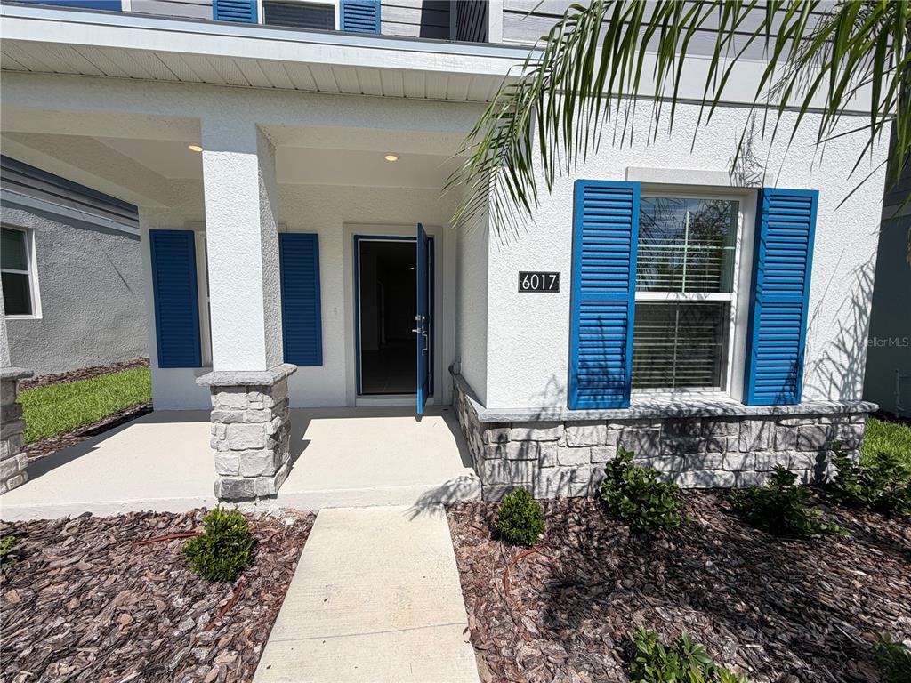 The exterior of a house features a covered porch, stone accents, and blue shutters — 6017 WELLBEING WAY, CLERMONT, FL