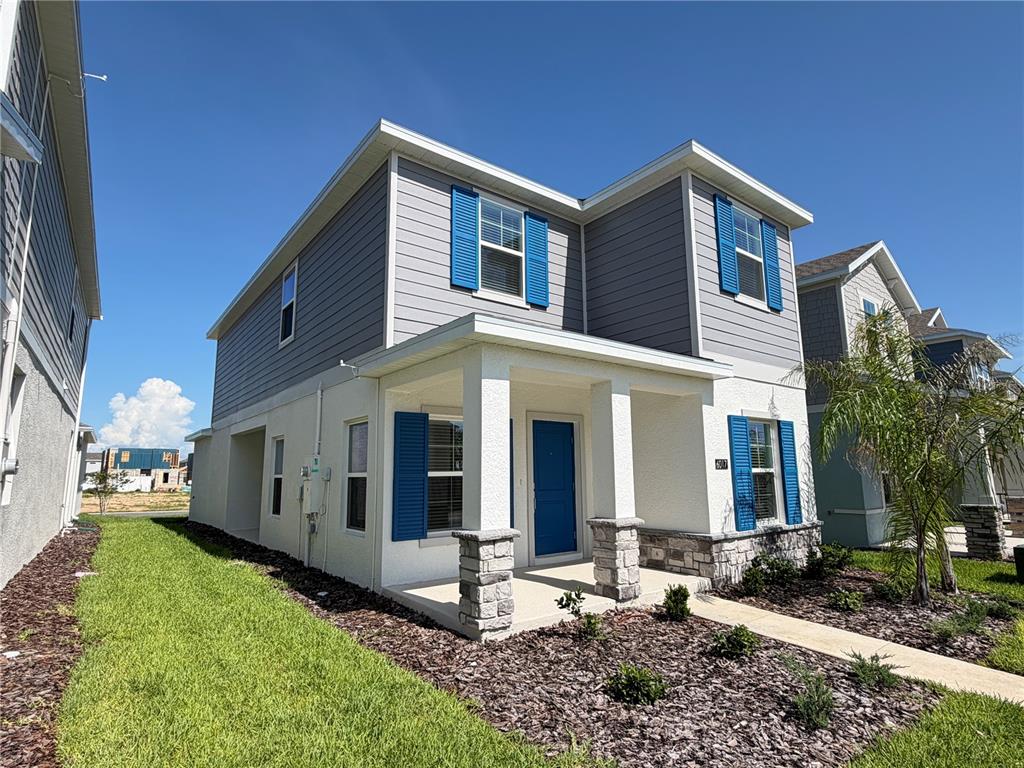 A two-story house with gray siding, blue shutters, and a covered front porch with stone pillars — 6017 WELLBEING WAY, CLERMONT, FL