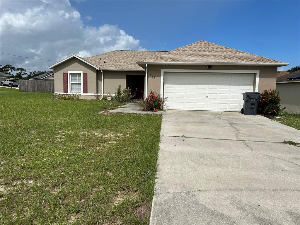 A single-story house with a beige stucco exterior, a two-car garage, and a concrete driveway — 128 INCONNU COURT, KISSIMMEE, FL