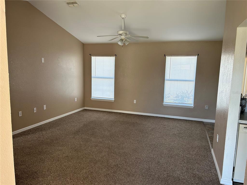 A carpeted living room with tan walls, a vaulted ceiling, and two windows — 128 INCONNU COURT, KISSIMMEE, FL