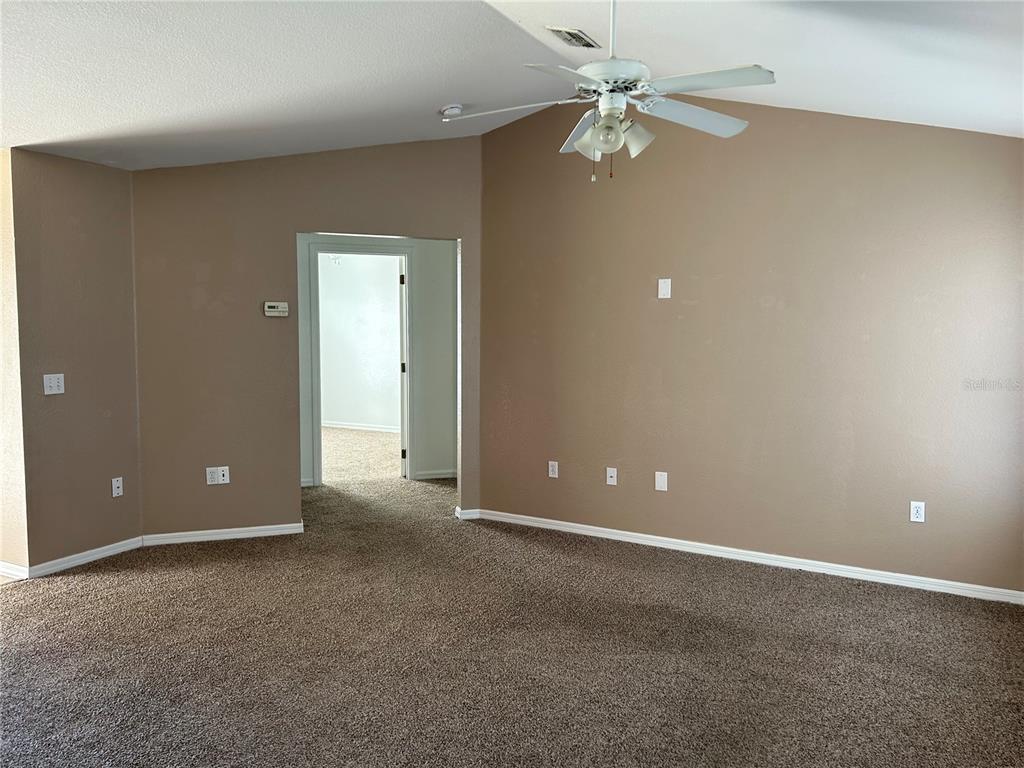 A carpeted living room features tan walls, a vaulted ceiling with a fan, and a doorway — 128 INCONNU COURT, KISSIMMEE, FL
