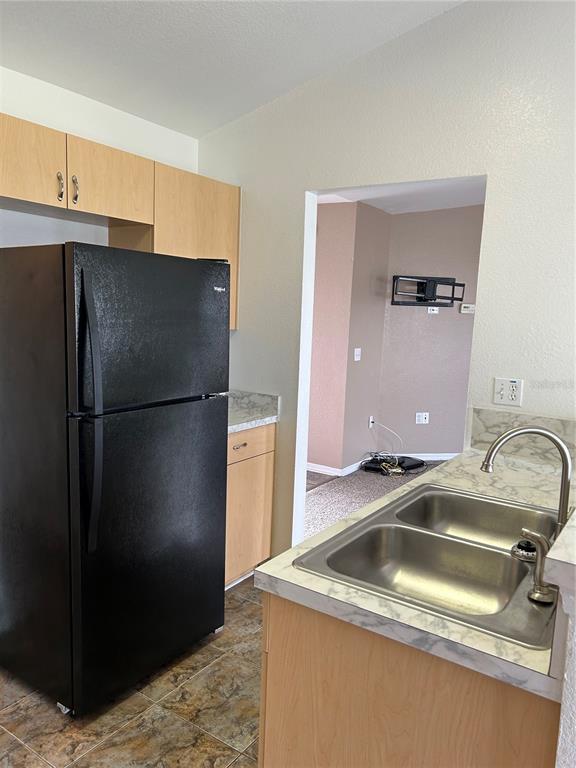 A kitchen features a black refrigerator, light wood cabinets, and a double-basin stainless steel sink — 128 INCONNU COURT, KISSIMMEE, FL