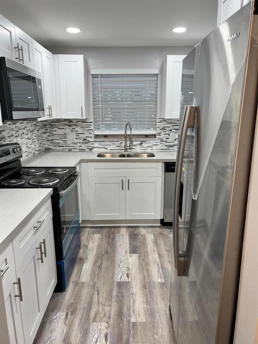 A kitchen features white cabinets, stainless steel appliances, a tiled backsplash, and wood-look flooring — 1340 NE 28th Avenue # 243, Pompano Beach FL 33062, POMPANO BEACH, FL